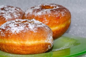 Sweet tasty donuts sprinkled with powdered sugar lie on a green glass plate, the national dish for the holiday of Hanukkah