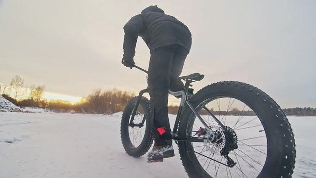 Professional extreme sportsman biker riding fat bike in outdoors. Cyclist ride in winter snow forest. Man does trial trick bike flip jump on mountain bicycle with big tire in helmet and glasses.