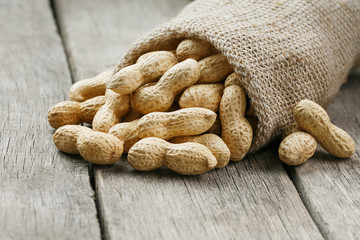 Peanuts in a miniature burlap bag on old, gray wooden surface