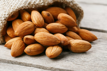 Almond nuts in a burlap bag on a wooden gray background.