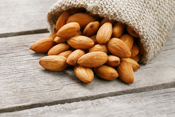 Almond nuts in a burlap bag on a wooden gray background.