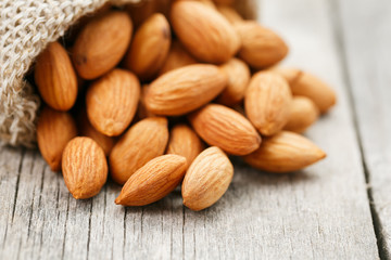 Almond nuts in a burlap bag on a wooden gray background.