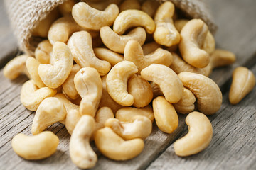 Cashew nuts in burlap bag on wooden gray background . Healthy food
