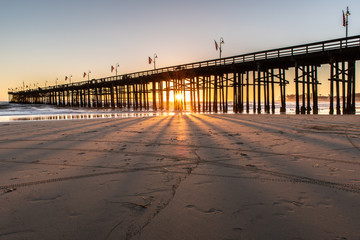 Obraz premium Sunset shining through the pier wooden pilings like spokes of a wagon wheel during this Autum Southern California evening.