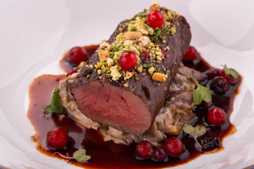 A stake the medium of roasting with a mushroom garnish in berry sauce with greens and nutlets