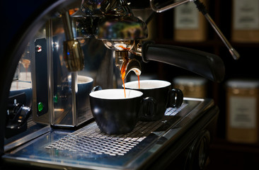 Coffee brewing in coffee machine. Espresso pouring in two cups. Shallow focus, dark blurred background.
