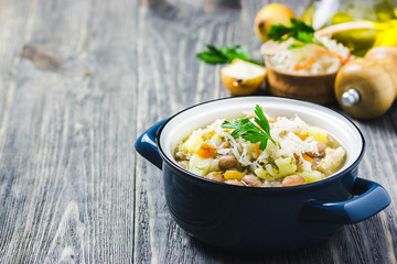 Sauerkraut soup with beans, vegetables and meat in a pot on wooden background. Selective focus, space for text.