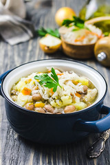 Sauerkraut soup with beans, vegetables and meat in a pot on wooden background. Selective focus, space for text.