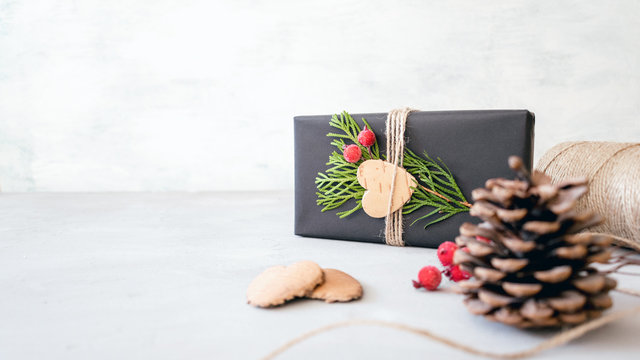 Wrapping Christmas gifts in recycled paper in rustic style. Xmas Gift boxes with craft paper, twine, coniferous branches, red berries and scissors on grey concrete background. Christmas gift pack