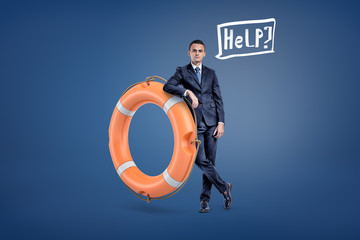 A businessman stands leaning on a large orange life buoy with a speech bubble holding a word Help inside.