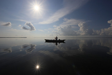 Kayaker on a calm Biscayne Bay, Florida, amidst cloud and sun reflections.