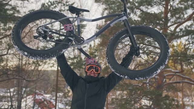 Professional extreme sportsman biker to bear fat bike to up mountain in outdoors. Cyclist walk in winter snow forest. Man walking with mountain bicycle with big tire in helmet, glasses. Slomo 60fps.