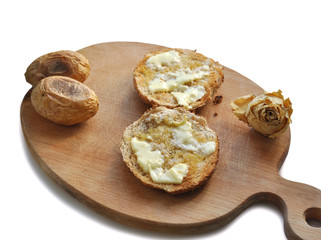Two Rounded Slices of Bread with Butter, two baked potatoes and a dry white rose on a Wooden Chopboard.