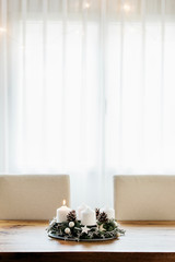 Lighting the first candle on the Advent Wreath on the first Sunday in December to celebrate the beginiing of Christmas holidays in Switzerland. Indoor table decoration, white curtains background.