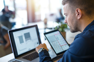 Business man looking and analyzing projects on his laptop computer and tablet. Elegant blonde hair...