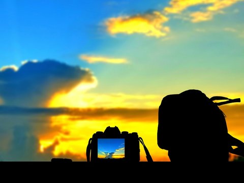 Silhouette digital camera and bag on table floor is recording with blur clouds and colorful sunrise sky background, technology and travel concept, illustration mode