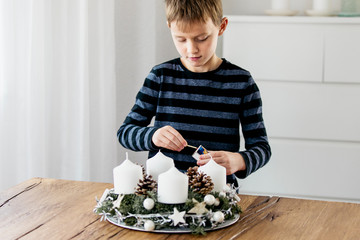 Young boy lighting the first candle on Advent Wreath on the first Sunday in December. Celebrating...