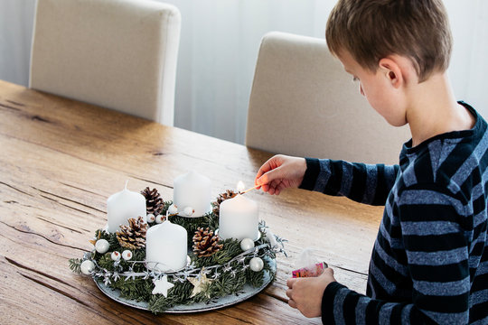 Young boy lighting the first candle on Advent Wreath on the first Sunday in December. Celebrating Christmas holidays, swiss tradition.