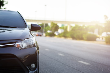 Focusing on the Dark Gray car headlights on a street corner with sunlight flares, In the background, the driver, bike and car. Closeup headlights of car. Copy space for insert text.