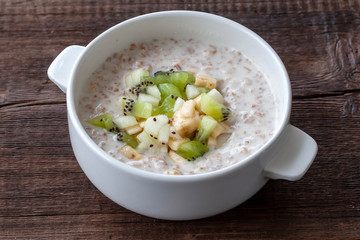 Vegetarian breakfast: milk oatmeal with banana, pear and kiwi slices