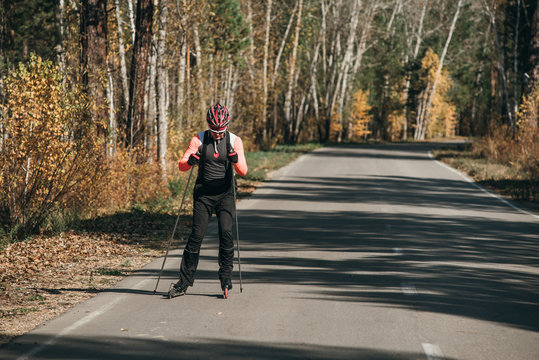 Training an athlete on the roller skaters. Biathlon ride on the roller skis with ski poles, in the helmet. Autumn workout. Roller sport. Adult man riding on skates.