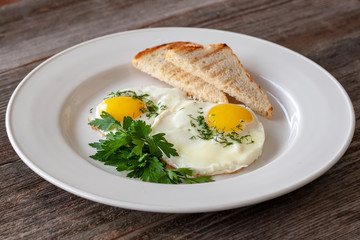 Vegetarian breakfast: fried eggs with greens and croutons on a white plate