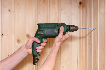 man's hands hold a drill and drill a wooden wall