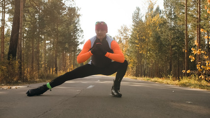 Training an athlete on the roller skaters. Biathlon ride on the roller skis with ski poles, in the helmet. Autumn workout. Roller sport. Adult man riding on skates. The athlete does the workout.