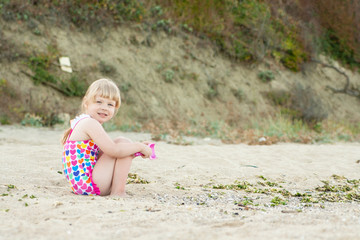 Child plays sitting on the sand at the beach on a sunny summer day. Happy little girl.