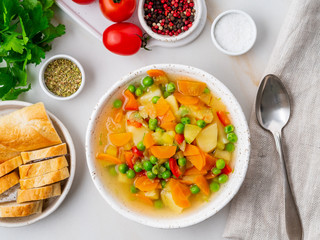 Vegetable soup, bright spring vegetarian dish. Carrots, potatoes, green peas. White light marble table, top view