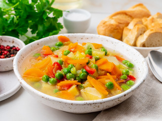 Vegetable soup, bright spring vegetarian dish. Carrots, potatoes, green peas. White light marble table, side view