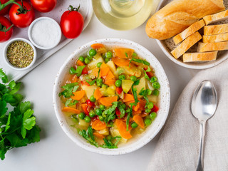 Vegetable soup, bright spring vegetarian dish. Carrots, potatoes, green peas. White light marble table, top view