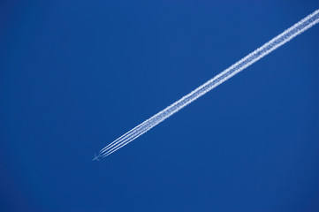 FOUR ENGINE JET AIRLINER WITH EXHAUST VAPOUR TRAILS IN CLEAR BLUE SKY