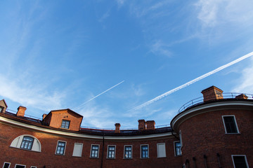 Белый след от самолета в голубом небе над крышей кирпичного здания
