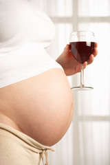 YOUNG PREGNANT WOMAN DRINKING GLASS OF RED WINE