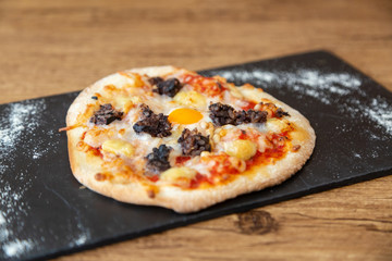 Close up of pizza on a blackboard with flour on a wooden table
