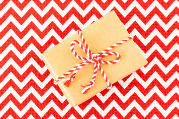 Christmas flat-lay of hand crafted gift box of kraft wrapping paper on red with white textile tablecloth.