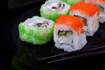 Fresh sushi rolls with cream cheese, rice, caviar and seafood against the black background. Asian cuisine meal