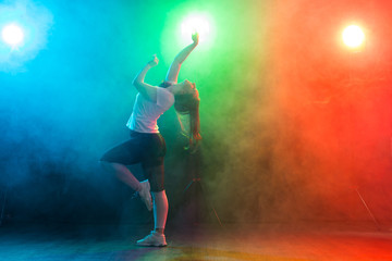 Fototapeta na wymiar Dance, sport, and people concept - young woman dancing in the darkness under colourful light