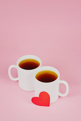 Red paper heart and two white cups on pink background. Valentine's day, love, wedding concept