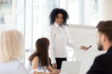 Smiling mixed race mentor gives presentation at diverse team office training explains sales growth...