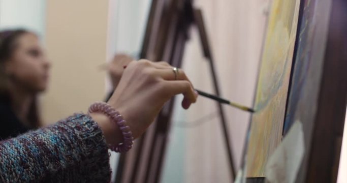 Young Beautiful Female Artist is in an Art Studio, Sitting Behind an Easel and Painting on Canvas. Drawing Process: in the Art Studio of the Artist's Hand Art Girl with a Brush Painting on Canvas.4K