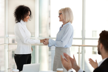Mature team leader female ceo congratulating happy successful african american office worker with promotion, smiling aged boss shaking hand of young mixed race employee excited by reward recognition