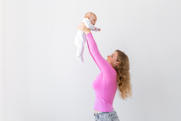 Motherhood, infant and people concept - mother throws baby up, laughing and playing with him on white background with copy space