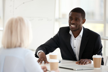 Smiling african american businessman mentor coach in suit speaking at office meeting discussing new...