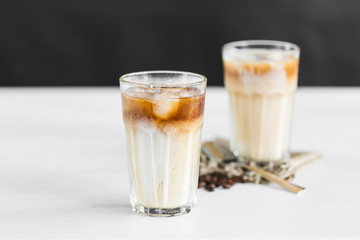 Ice coffee in a glass with cream over and coffee beans on the table