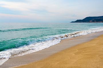 Waves with foam hitting sand on Kleopatra beach in Alanya, Turkey on a sunset against a cloudy sky.  