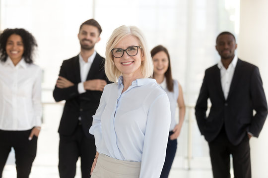 Portrait of happy older woman middle aged company ceo, female corporate leader mentor looking in camera with team subordinates, friendly mature executive boss, hr or business coach posing in office