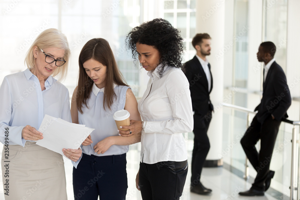 Canvas Prints mature team leader and young female employees discussing paperwork standing in office, diverse emplo