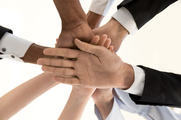 Obraz premium Diverse business people team hands joined in pile stack as concept of corporate unity support, multi-ethnic employees group engage in teambuilding, promising loyalty help, close up below bottom view